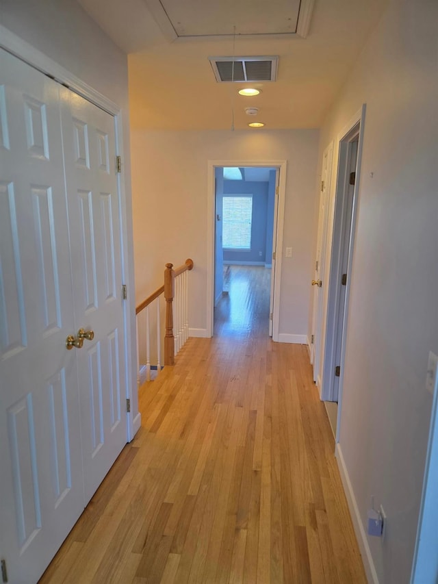 hallway featuring visible vents, an upstairs landing, baseboards, light wood-type flooring, and attic access