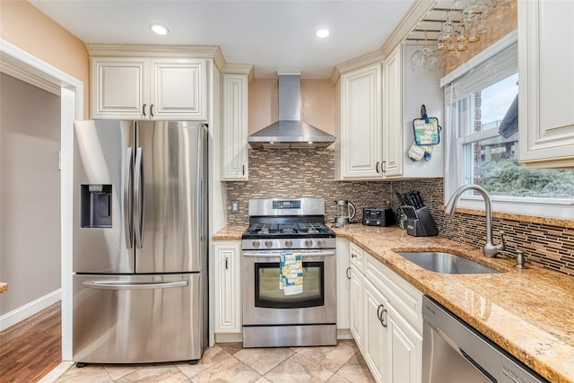 kitchen with backsplash, appliances with stainless steel finishes, a sink, wall chimney range hood, and light stone countertops