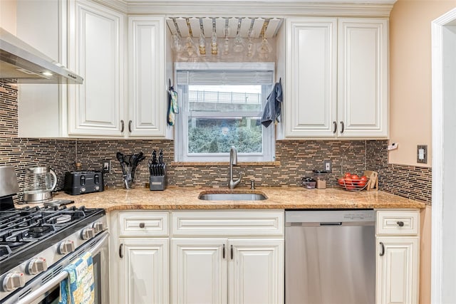 kitchen with wall chimney range hood, appliances with stainless steel finishes, decorative backsplash, and a sink