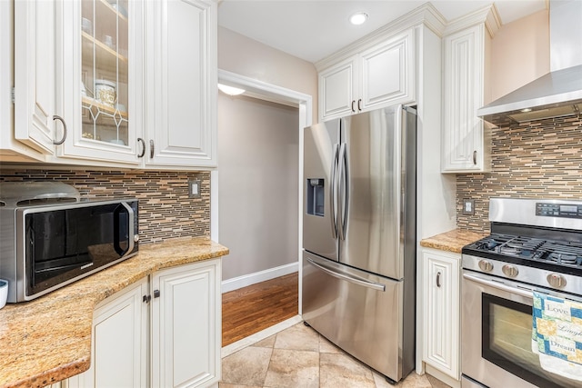 kitchen featuring wall chimney range hood, glass insert cabinets, appliances with stainless steel finishes, and white cabinetry