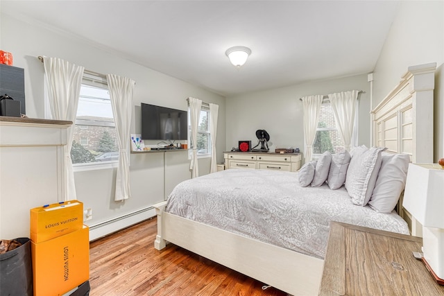 bedroom with a baseboard heating unit and light wood finished floors