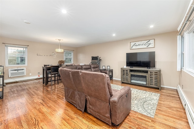 living room featuring a wall unit AC, a baseboard radiator, baseboards, light wood-type flooring, and plenty of natural light