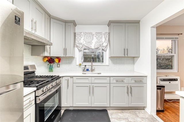 kitchen featuring appliances with stainless steel finishes, a sink, light countertops, gray cabinetry, and backsplash