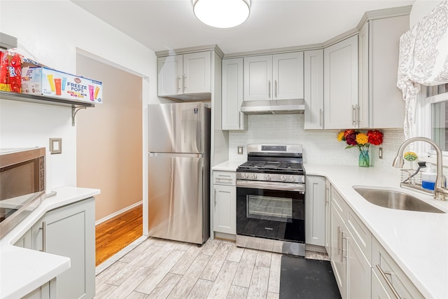 kitchen with light wood finished floors, appliances with stainless steel finishes, light countertops, under cabinet range hood, and a sink