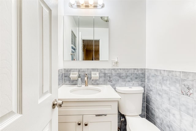 half bath with tile walls, wainscoting, vanity, and toilet