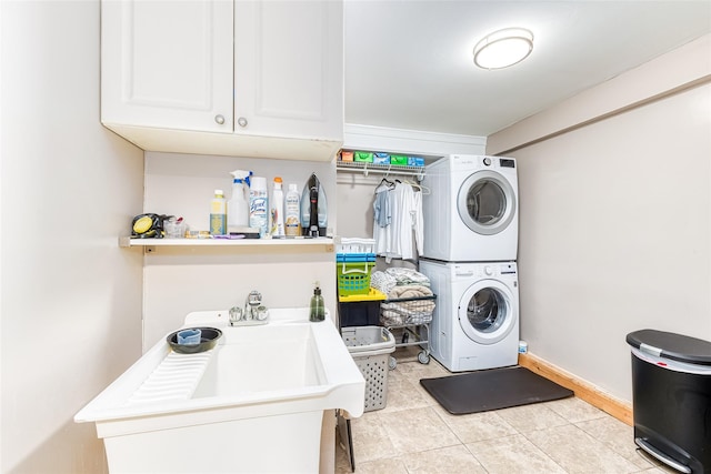 clothes washing area featuring stacked washer and dryer, baseboards, and light tile patterned flooring