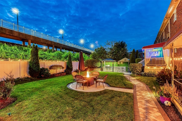 yard at dusk featuring a fire pit, a patio area, and fence