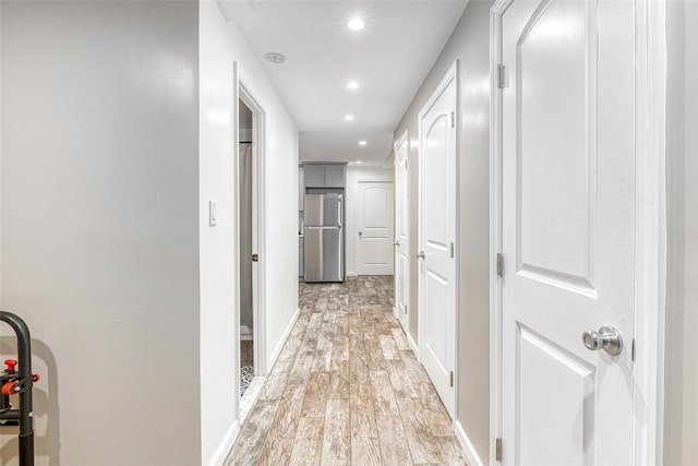 hallway featuring light wood finished floors, baseboards, and recessed lighting