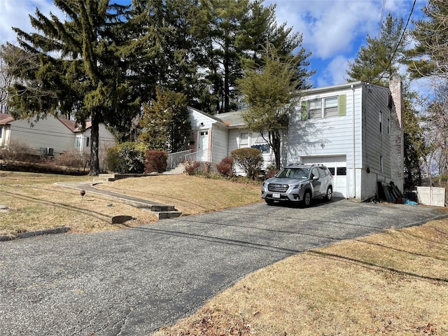 view of front of property with aphalt driveway, a front lawn, a chimney, and a garage