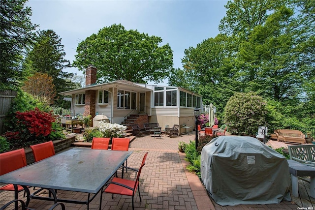 rear view of house with entry steps, a patio, a sunroom, outdoor dining space, and a chimney