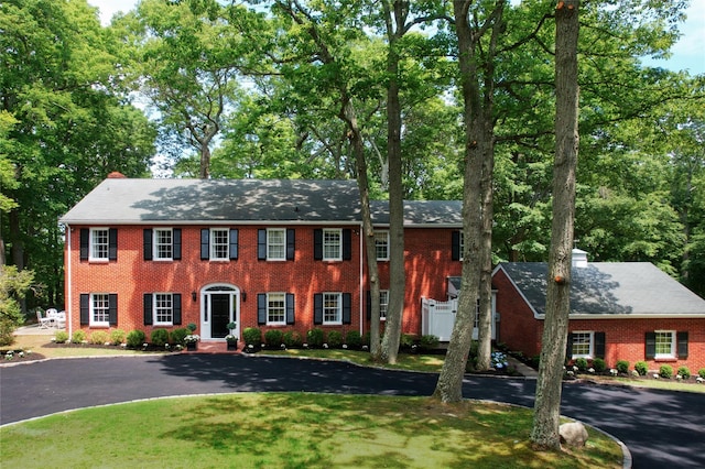 colonial house featuring brick siding, driveway, and a front lawn