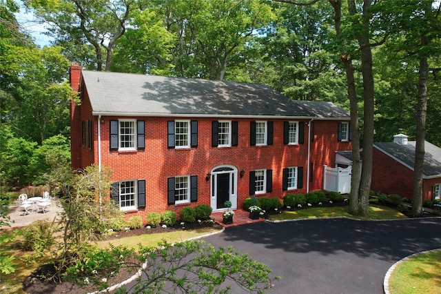 colonial-style house featuring brick siding, driveway, and a chimney