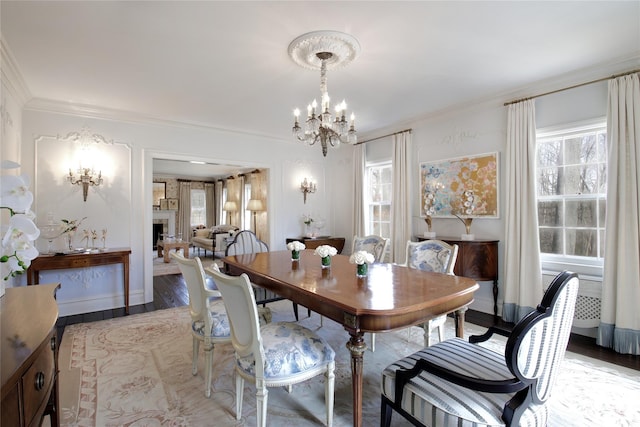 dining area with a notable chandelier, a fireplace, baseboards, light wood-type flooring, and crown molding