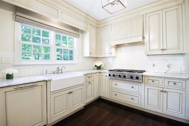 kitchen featuring light stone counters, custom exhaust hood, stainless steel gas stovetop, cream cabinets, and a sink