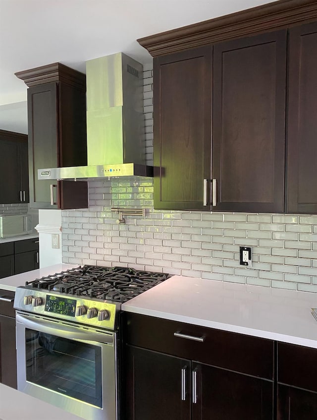 kitchen with dark brown cabinetry, light countertops, wall chimney range hood, decorative backsplash, and stainless steel gas stove