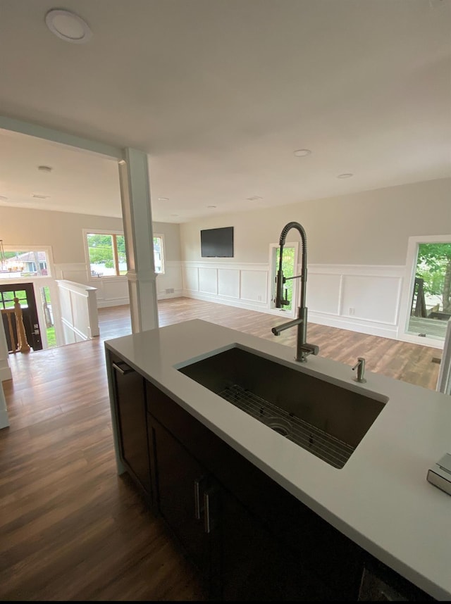 kitchen with dark wood-style floors, a wainscoted wall, light countertops, open floor plan, and a sink