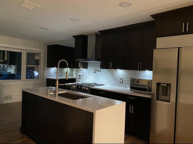 kitchen with visible vents, light countertops, appliances with stainless steel finishes, wall chimney range hood, and a center island with sink