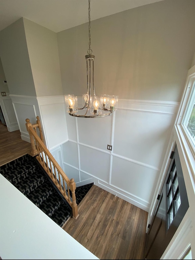 stairs with a notable chandelier, wainscoting, wood finished floors, and a decorative wall