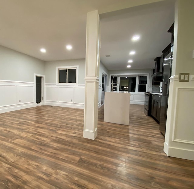 interior space with decorative columns, open floor plan, dark wood finished floors, and a decorative wall