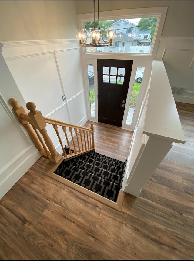 foyer entrance featuring dark wood-style flooring, a notable chandelier, a decorative wall, a towering ceiling, and stairs