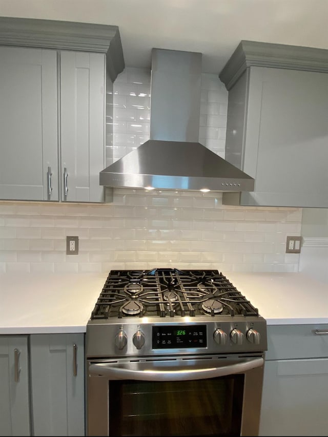 kitchen with gas stove, light countertops, wall chimney range hood, and decorative backsplash