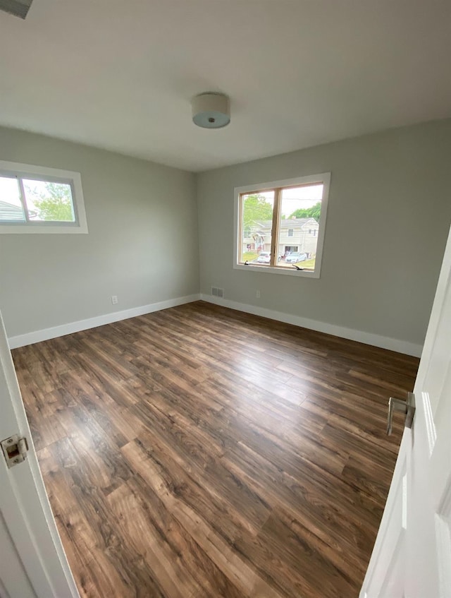 unfurnished room featuring dark wood-type flooring, visible vents, plenty of natural light, and baseboards