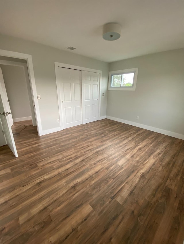 unfurnished bedroom with visible vents, baseboards, dark wood finished floors, and a closet