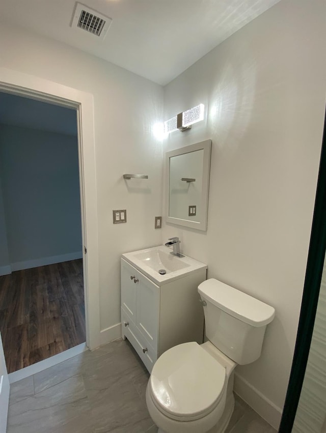 bathroom featuring toilet, vanity, visible vents, and baseboards