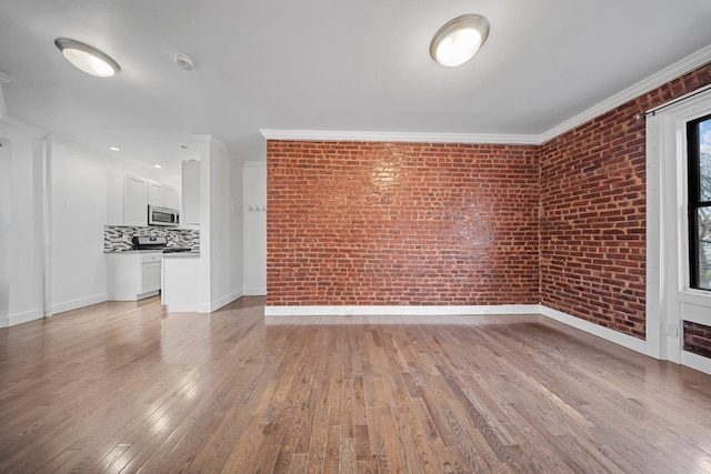 empty room with light wood finished floors, brick wall, and crown molding