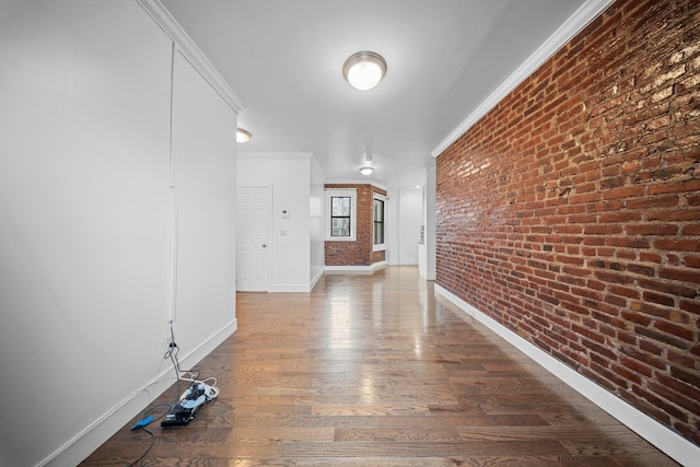 hallway featuring baseboards, brick wall, ornamental molding, and wood finished floors