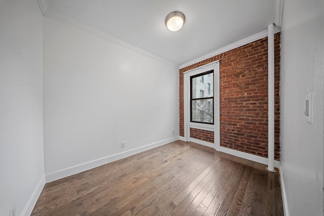 unfurnished room with brick wall, wood-type flooring, baseboards, and crown molding