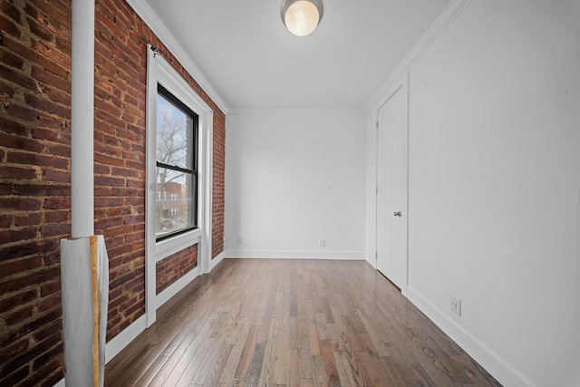 spare room with hardwood / wood-style flooring, brick wall, baseboards, and ornamental molding