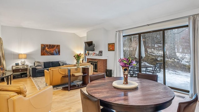 dining space with lofted ceiling, light wood-style floors, a brick fireplace, and visible vents