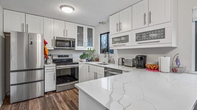 kitchen with glass insert cabinets, appliances with stainless steel finishes, white cabinets, and light stone counters