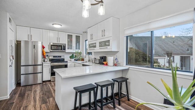 kitchen featuring a peninsula, a sink, white cabinetry, appliances with stainless steel finishes, and dark wood-style floors