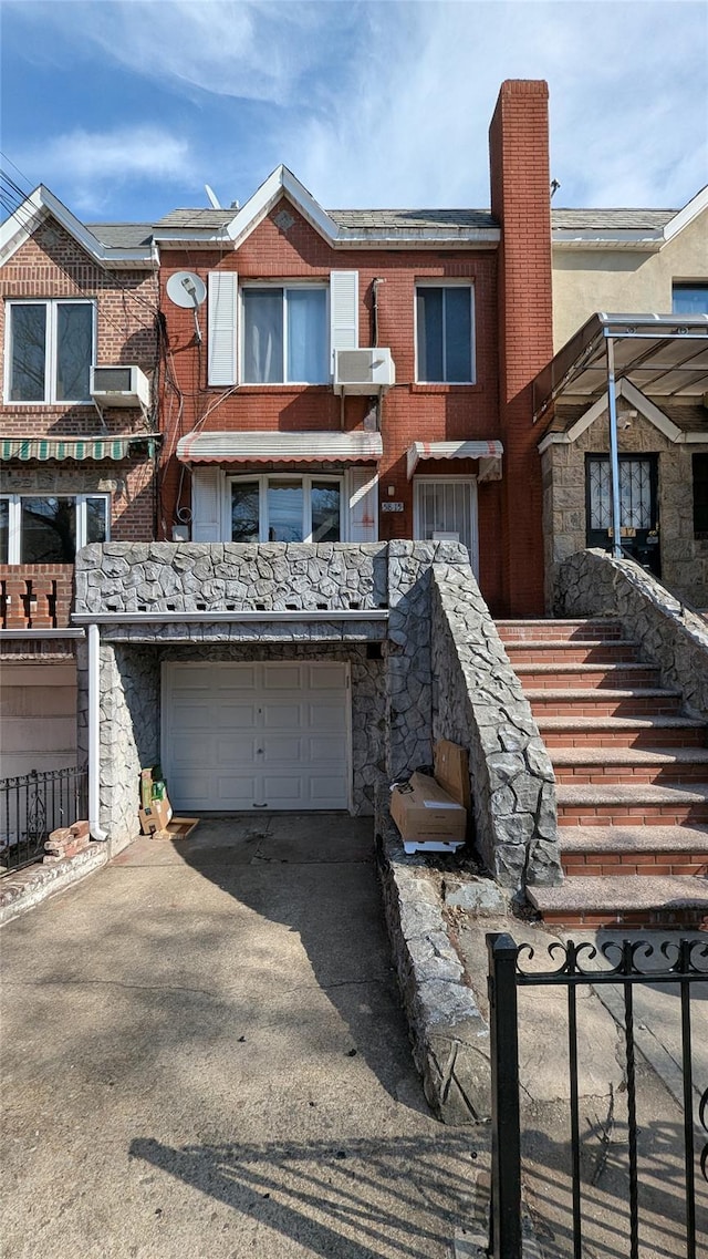 multi unit property with driveway, stone siding, a chimney, an attached garage, and brick siding