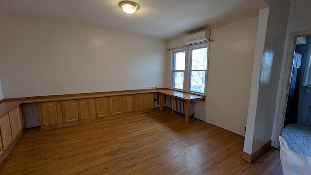 spare room with crown molding, built in desk, radiator, an AC wall unit, and wood finished floors