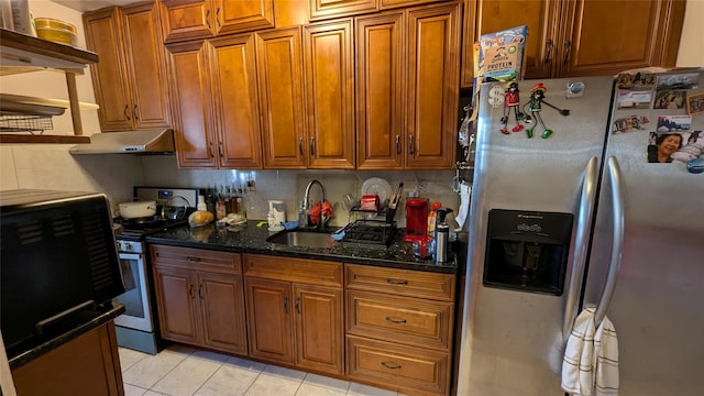 kitchen with dark stone counters, brown cabinetry, stainless steel appliances, under cabinet range hood, and a sink