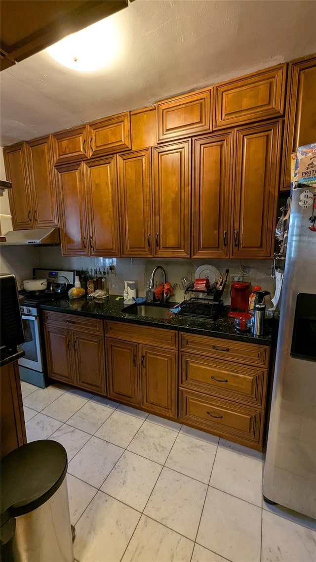 kitchen with brown cabinets, dark stone countertops, stainless steel appliances, under cabinet range hood, and a sink