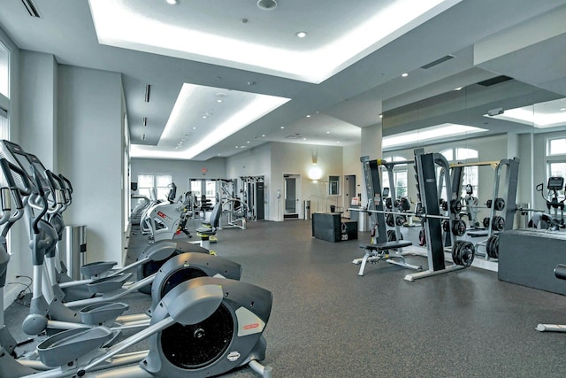 exercise room with a tray ceiling, plenty of natural light, and visible vents