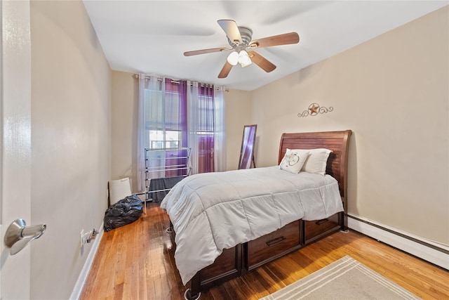 bedroom featuring a baseboard heating unit, ceiling fan, hardwood / wood-style flooring, and baseboards