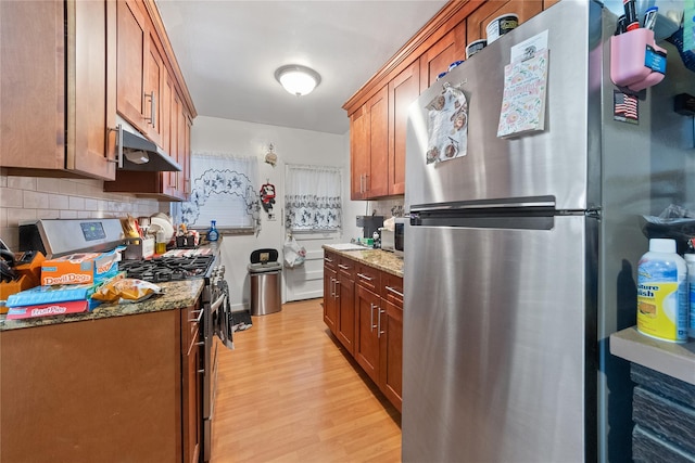 kitchen featuring tasteful backsplash, light wood-style flooring, stone counters, stainless steel appliances, and under cabinet range hood