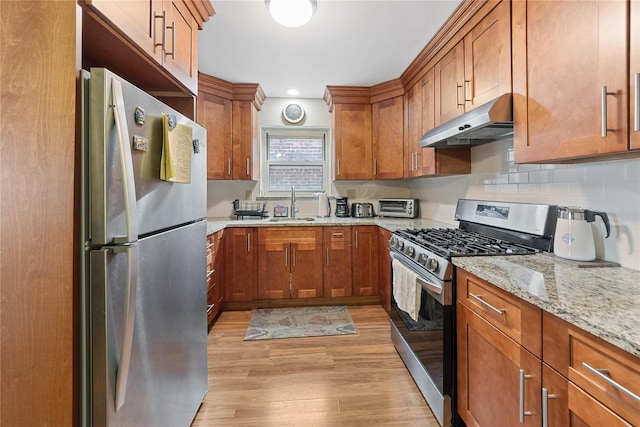 kitchen with brown cabinets, light wood-style flooring, appliances with stainless steel finishes, a sink, and under cabinet range hood