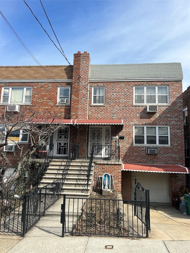 multi unit property with concrete driveway, a fenced front yard, a chimney, an attached garage, and brick siding