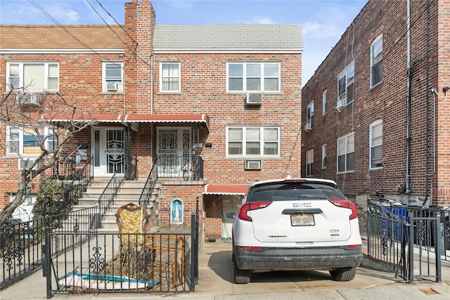 view of property featuring brick siding, a fenced front yard, a chimney, and a wall mounted AC