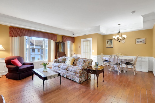 living area with a wainscoted wall, ornamental molding, a raised ceiling, and light wood-style floors