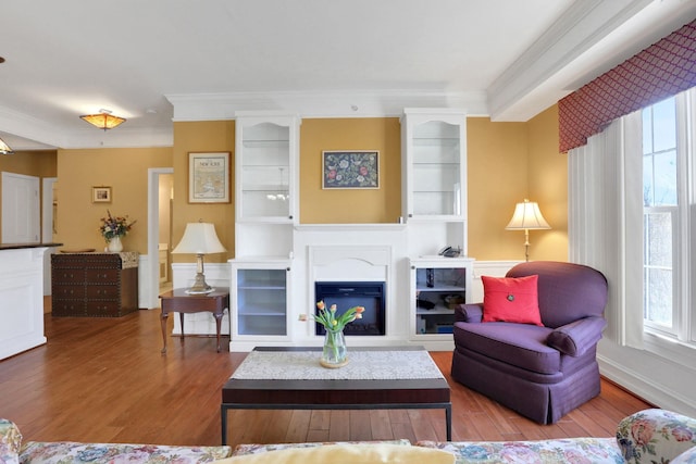 living area featuring ornamental molding, wood finished floors, a glass covered fireplace, and built in features