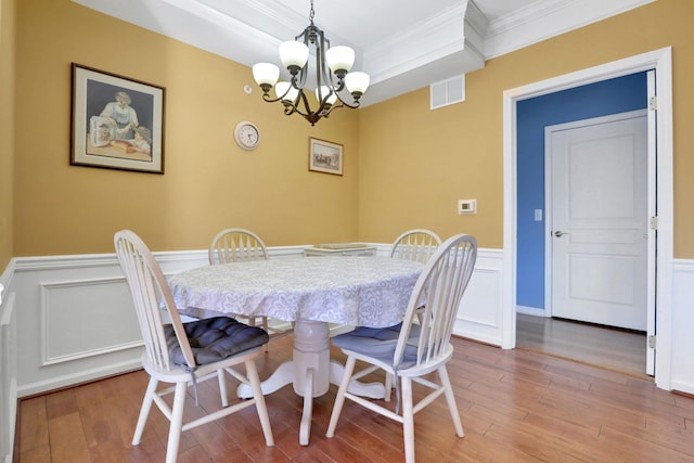 dining area with a wainscoted wall, visible vents, ornamental molding, wood finished floors, and a chandelier