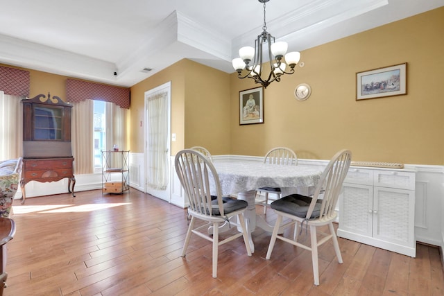 dining room with a wainscoted wall, ornamental molding, light wood-type flooring, a raised ceiling, and an inviting chandelier