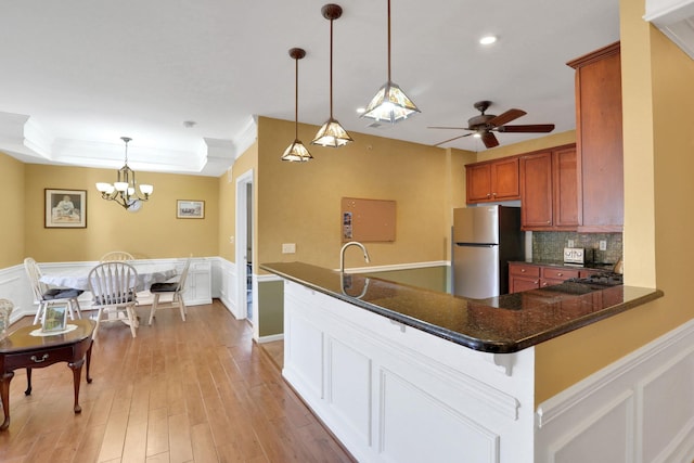 kitchen featuring brown cabinets, crown molding, light wood-style flooring, decorative backsplash, and freestanding refrigerator